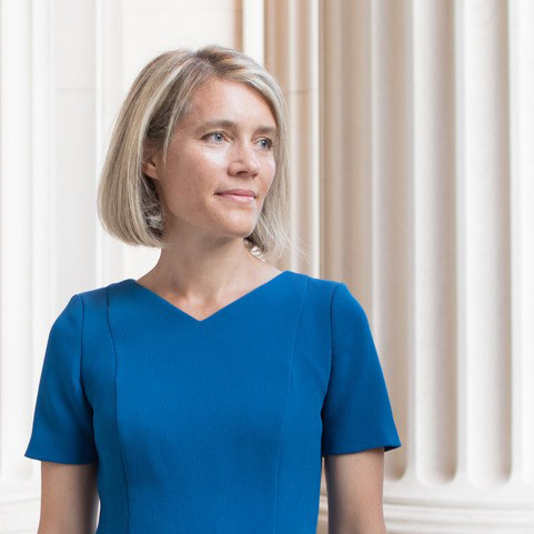 Jessica Trancik stands wearing a blue dress in front of several large white columns. 